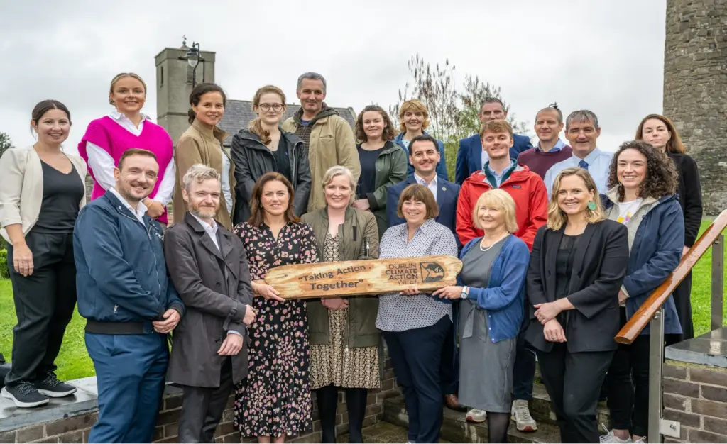 A large group of people stand together smiling at the camera and hold a sign for dublin climate action week