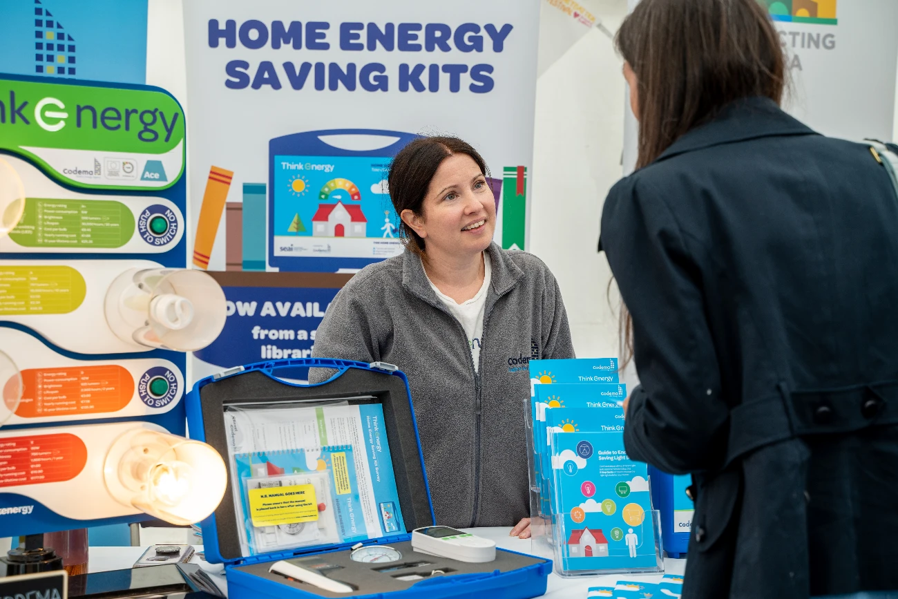 Codema staff member at a Home Energy Saving Kits display stand smiling at a person in front of the stand