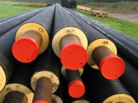 Image of large district heating pipes piled up. They are black on the outside with yellow foam and a red centre