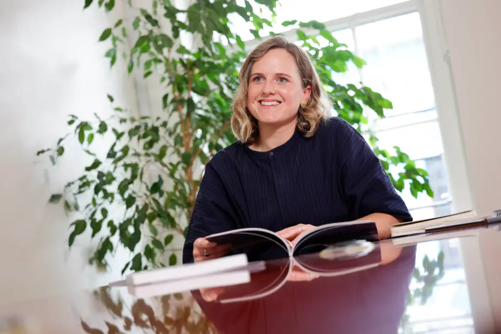 Codema staff member. A woman sits at a desk smiling with a report open in front of her and a plant behind her.