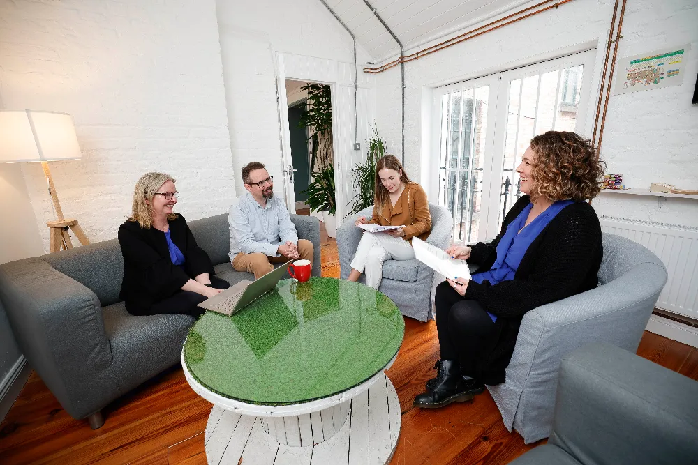 Codema staff members in a meeting room. Three women and a man sit on couches and arm chairs around a small table