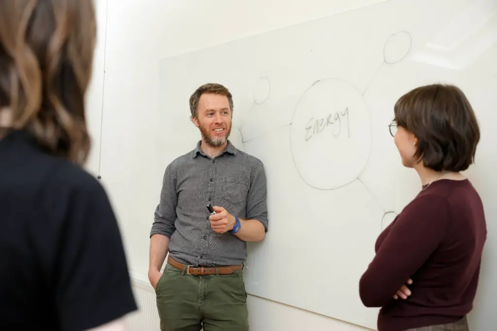 Image of Codema staff members standing at a whiteboard, A man is in focus holding a whiteboard marker, the whiteboard says 'energy'