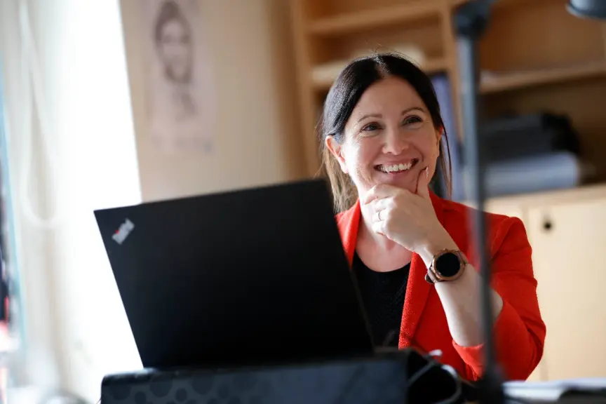 A Codema staff member wearing red sits at a laptop smiling