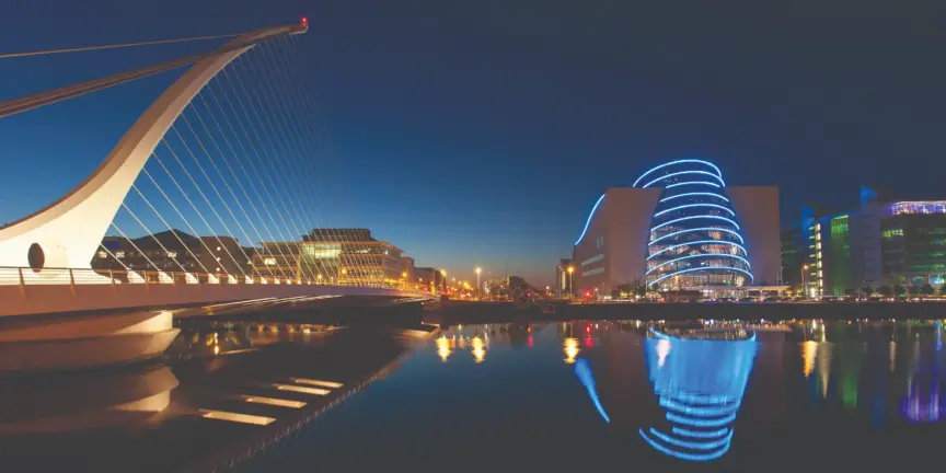 Photo of the Samual Beckett Bridge and the convention centre lit up at night reflecting on the River Liffey