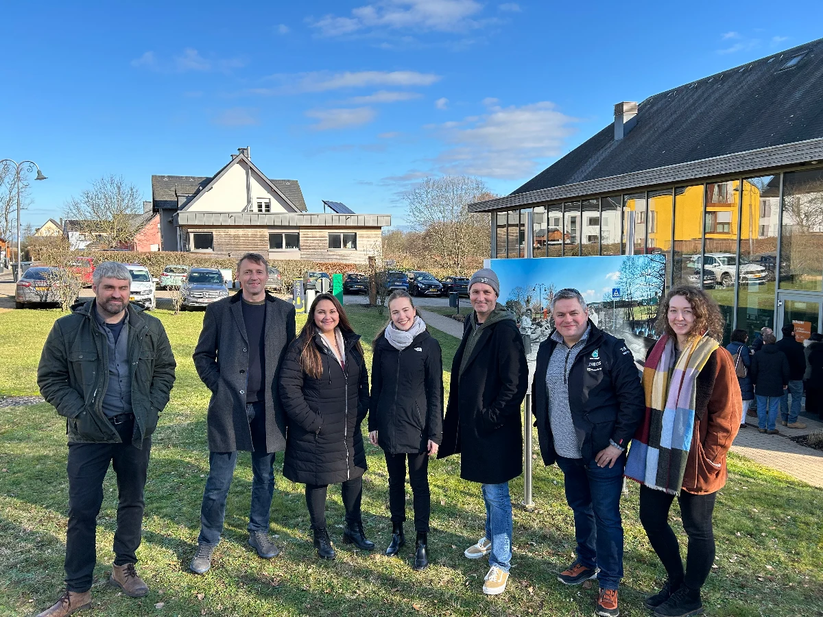 A group of people stand on the grass and smile at the camera with blue skies in the background