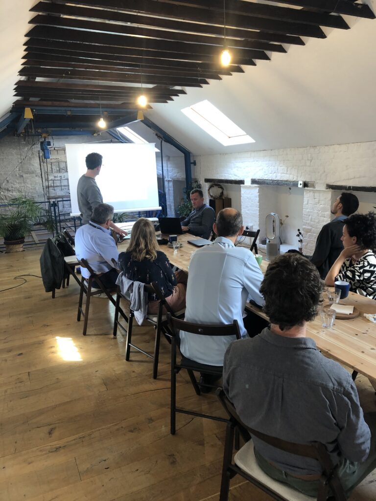 Image from behind of a group of people sitting at a long table watching a presentation