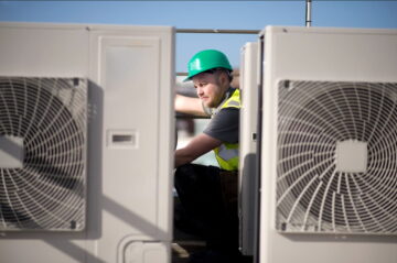 A worker in a high vis vest and hard hat crouching in between heat pumps